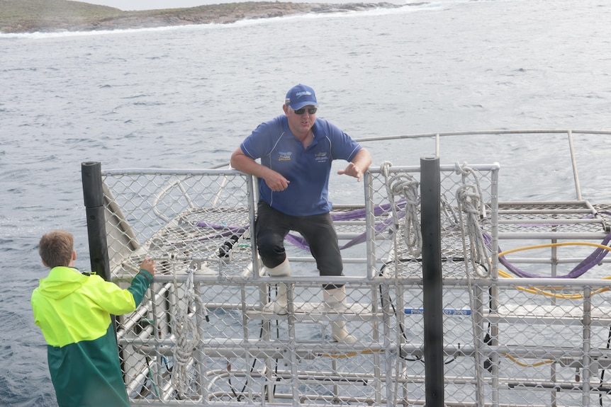 A man standing on a steel cage in the water.