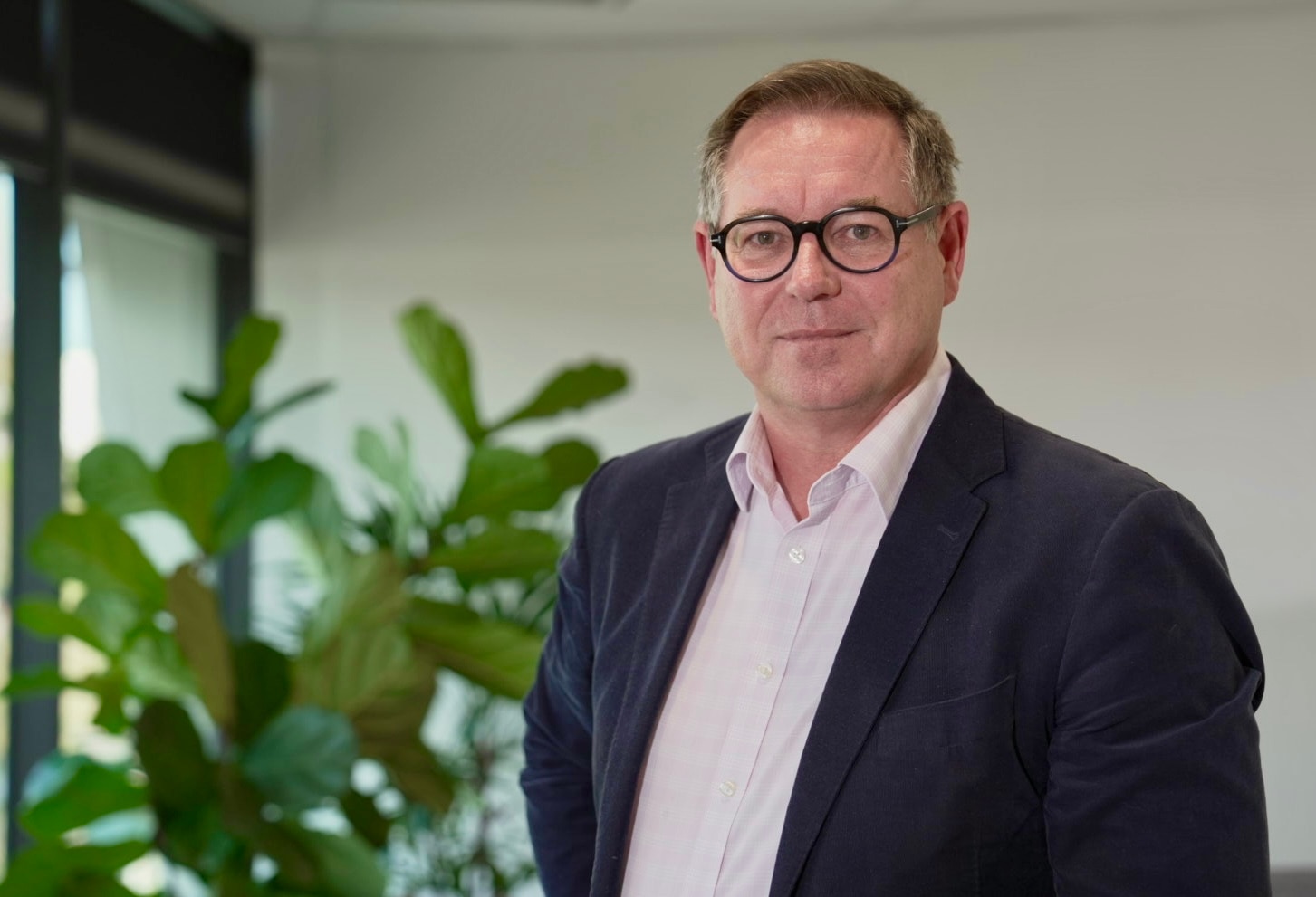 Um homem branco de meia-idade, com cabelo curto e óculos, em pé em um escritório