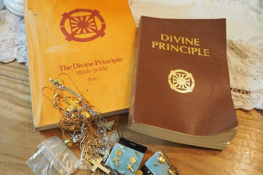 Two books laying flat on a table with some jewellery, including a crucifix, draped over the top