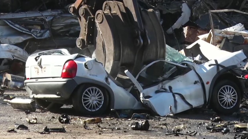 A white car is crushed with a bulldozer claw.