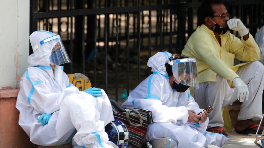 Two women in PPE sit on the ground outside a mortuary.