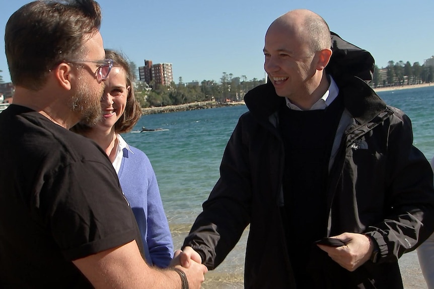 two men and a woman standing on the sand at the beach