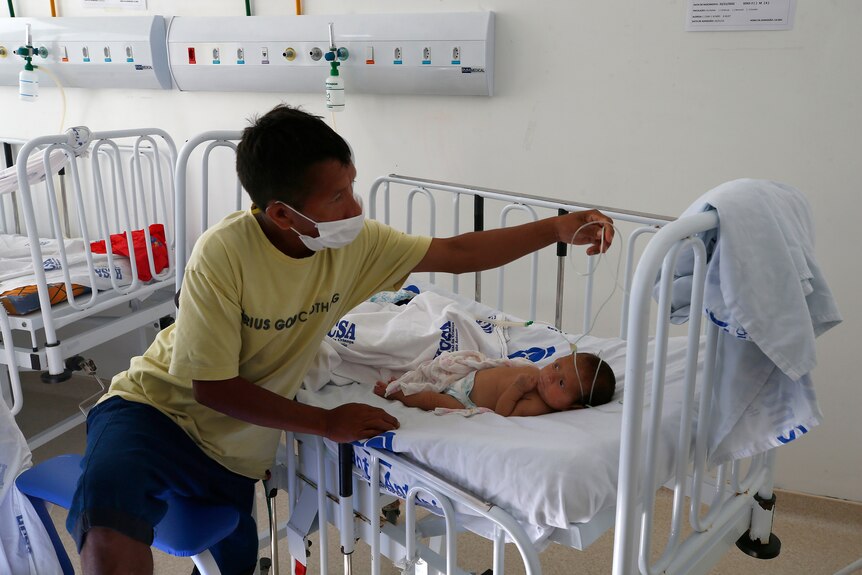 a man in a mask adjusts a tubing connected to a baby in a hospital bed