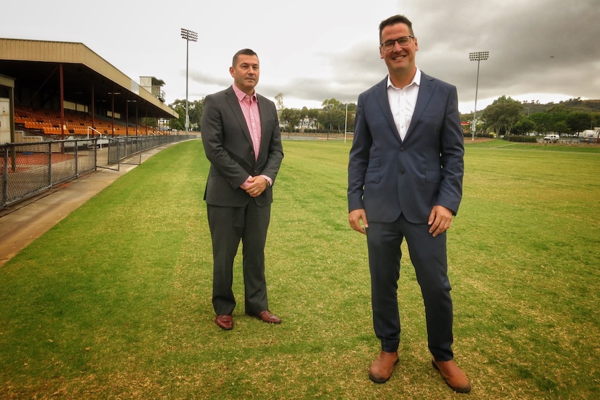 Two men in suits stand on a sporting field.