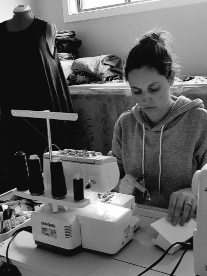 A black and white photo of a woman with brown hair, in a hoodie, working at a sewing machine.