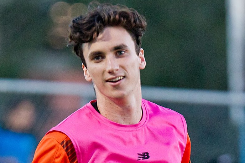 Henry Hore smiles and turns wearing a pink bib over an orange kit