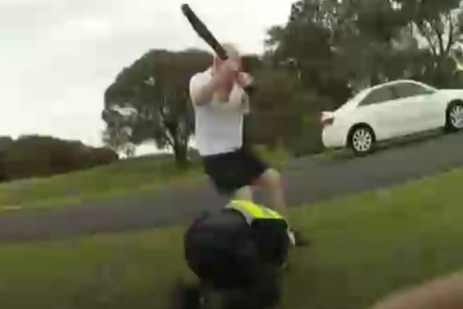 man in white tshirt armed with a metal baseball bat attacks a police officer crouching on ground.
