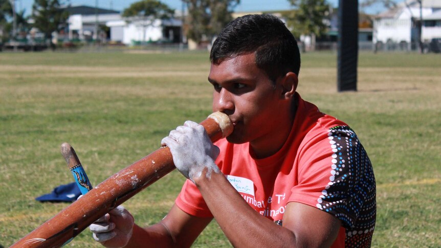 Young Indigenous man seated on ground playing the didgeridoo