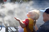 A little girl is held up to enjoy the misting fan