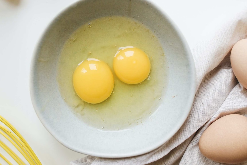 Two raw eggs in a bowl with a whisk, uncooked egg dishes have a higher risk of causing food poisoning.