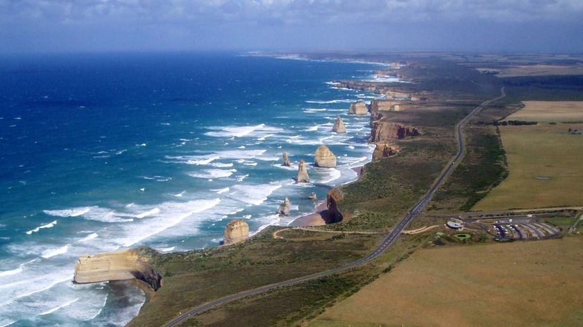 An aerial shot of a coastline bordered by a road running past some notable geographic features jutting out of the ocean.