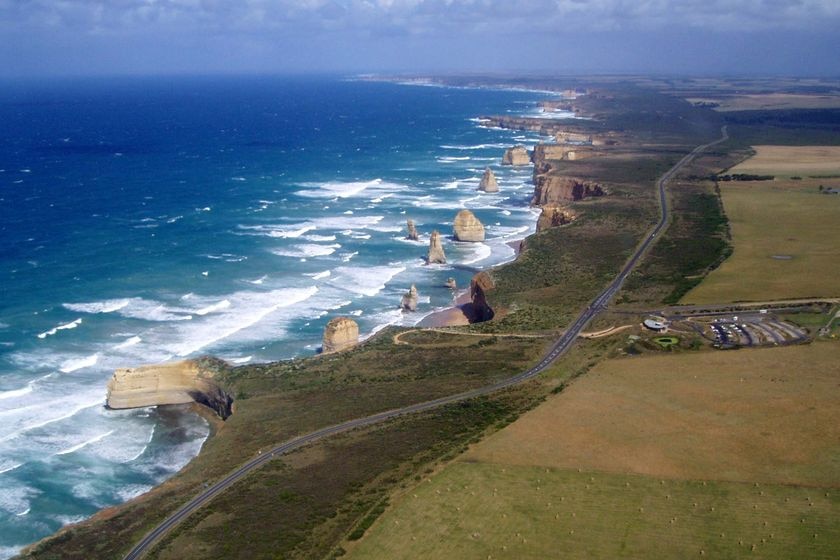 An aerial shot of a coastline bordered by a road running past some notable geographic features jutting out of the ocean.