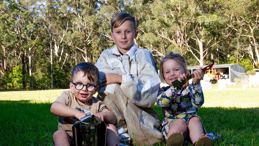 Three children posing for a photo holding bee keeping tools