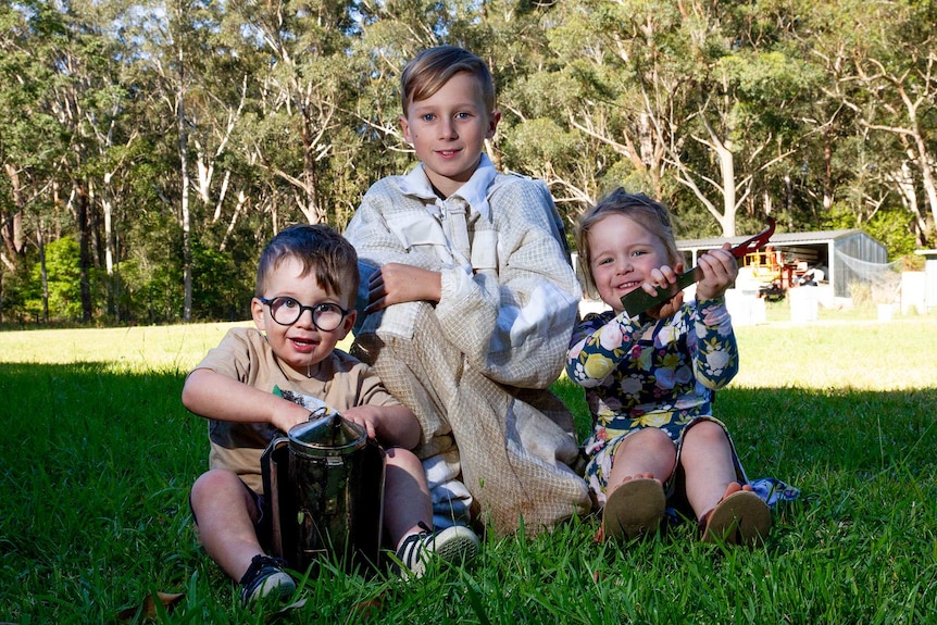 Three children posing for a photo holding bee keeping tools