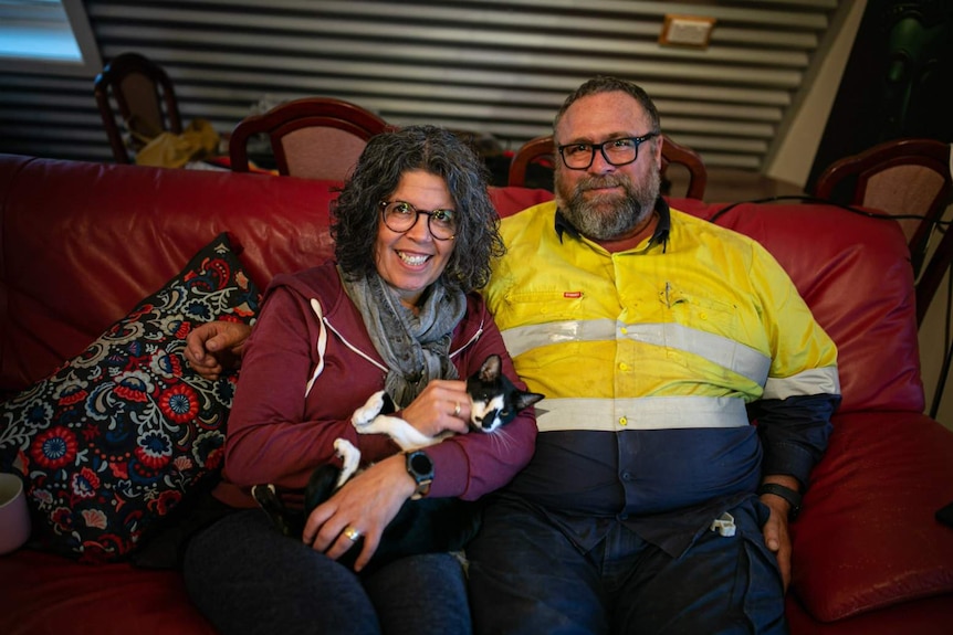 A man and a woman sit on a lounge and the woman is holding a cat.