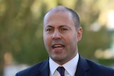 Josh Frydenberg wearing a navy suit with a maroon and blue tie and an Australia pin.