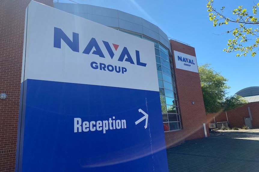 A blue and white sign reading Naval Group with a brown and glass building behind