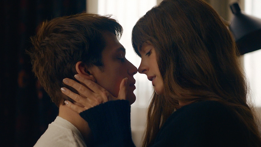 A film still of Nicholas Galitzine, 29, and Anne Hathaway, 41. They're about to kiss, Hathaway has her hand on his neck. 