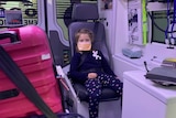 Six-year-old girl sits in ambulance with a face mask over her face.