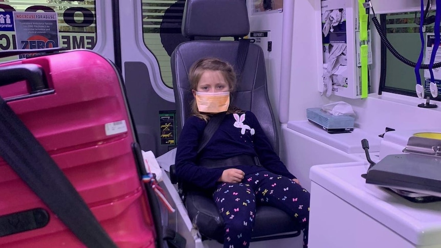 Six-year-old girl sits in ambulance with a face mask over her face.