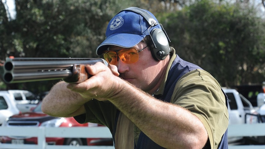 man in blue cap and orange glasses holding a rifle in shooting position