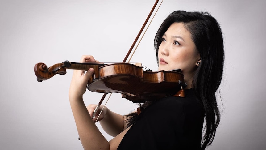 Emily Sun plays a violin in front of a white background. 