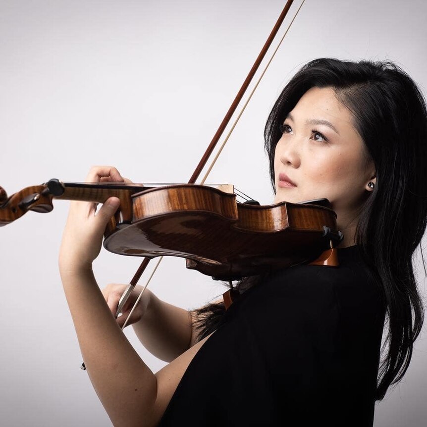 Emily Sun plays a violin in front of a white background. 