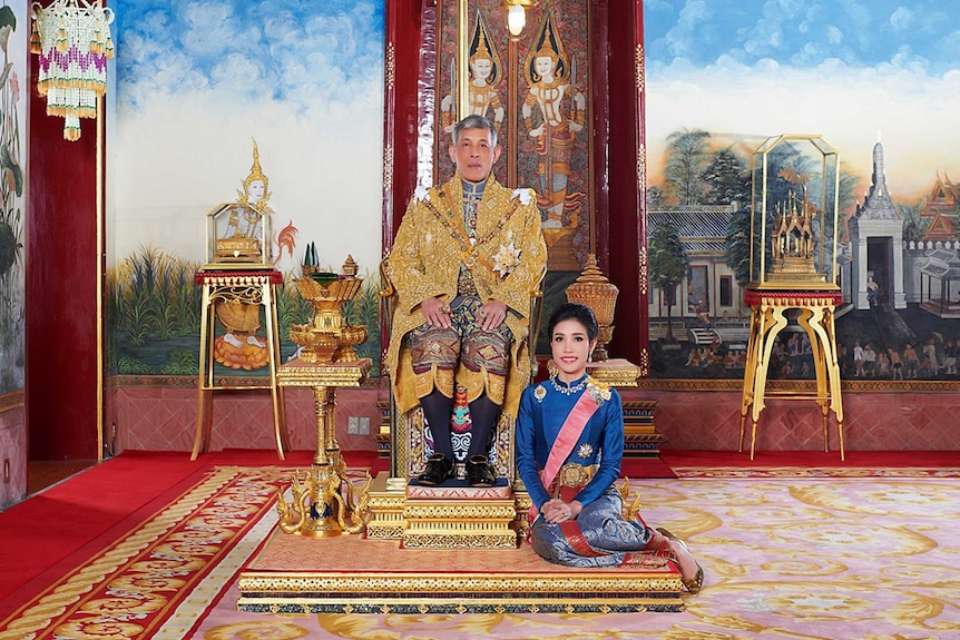 Sineenat is dressed in blue silk royal attire and sits at the feet of the king, dressed in gold and sits on the palace throne