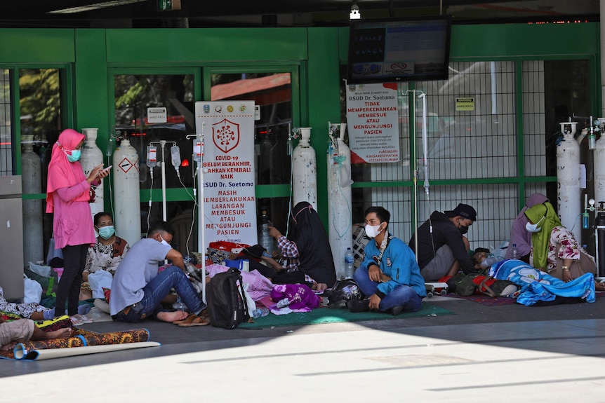 People sit on the floor outside the emergency ward of a hospital that cannot take any more patients