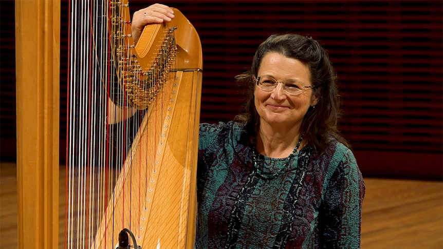 Alice Giles sits with her arm holding the top of her harp. She wears a green and purple snakeskin pattern top.