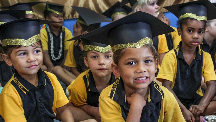 Four prep students dressed in glittery mortarboards smile at the camera during their graduation ceremony.