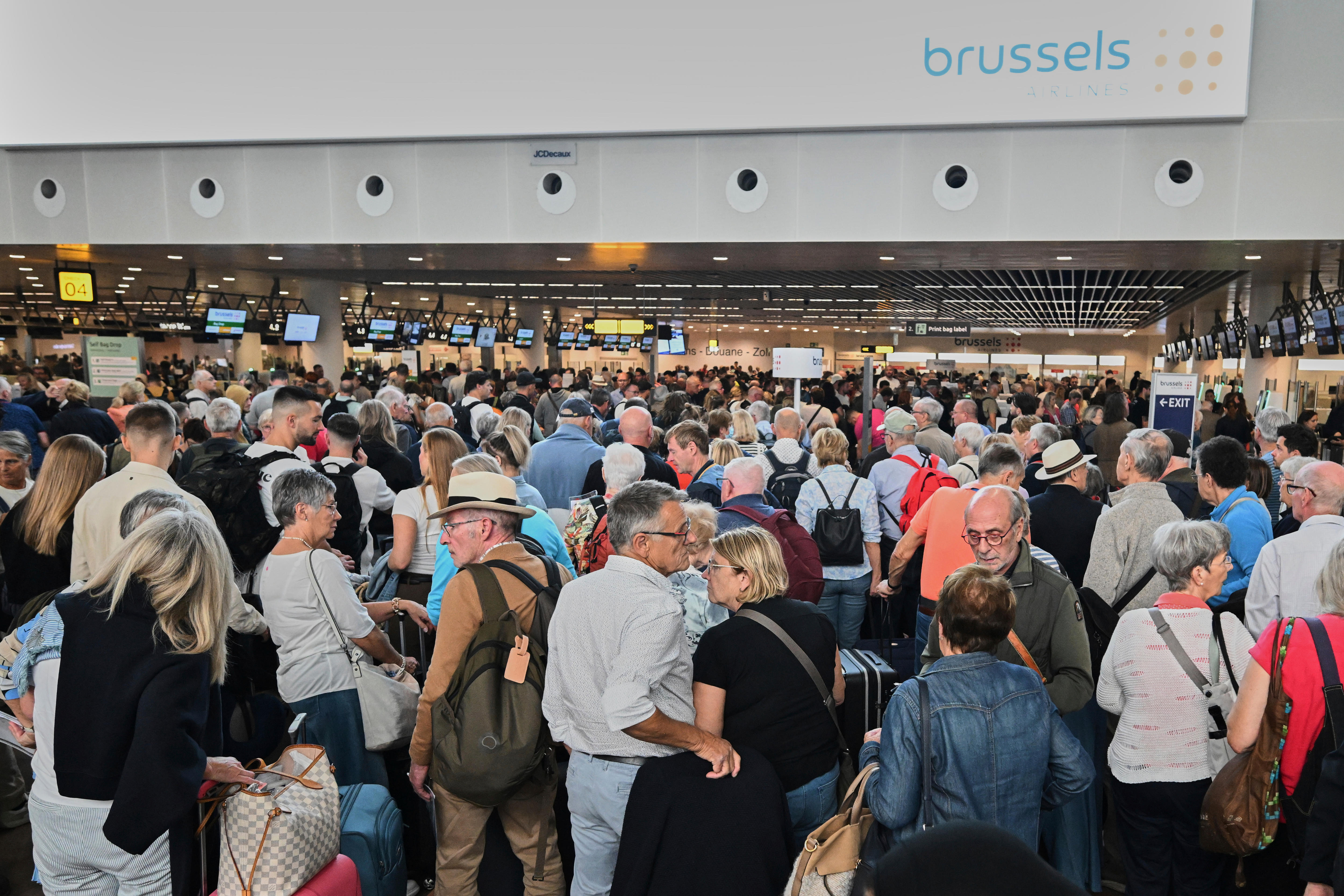 People stand in a line to check in after a cyber attack caused delays at Brussels airport
