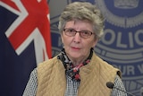 Ann standing in front of microphones, short grey hair, wearing glasses.