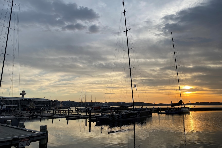 The sun rises over several yachts docked on Hobart's waterfront.