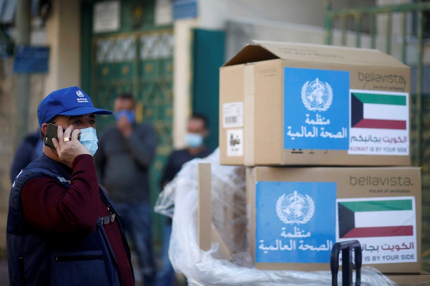 A man stands on the phone next to boxes with the WHO logo and Arabic writing