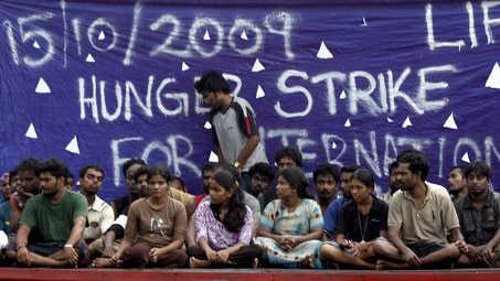 Detained Sri Lankan asylum seekers sit in their wooden boat next to an Indonesian navy ship