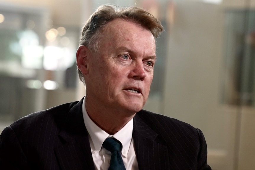 A man wearing a black suit talks at an event.