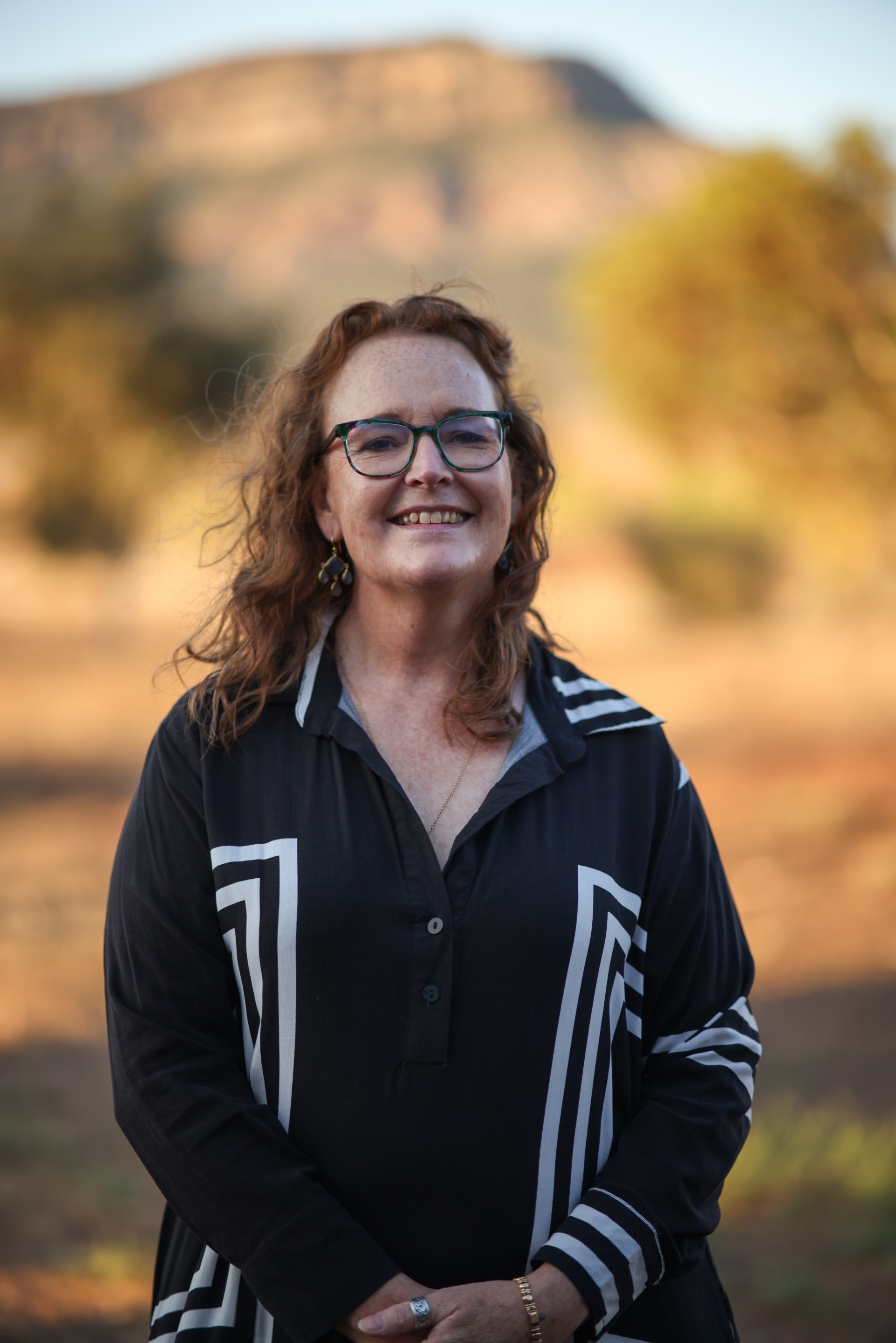 Una mujer con gafas sonríe a la cámara, tomada al aire libre