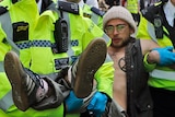 Three police officers carry a man from a large crowd of protesters