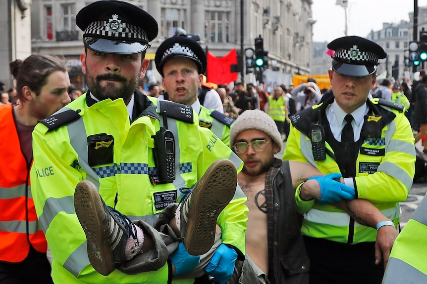 Three police officers carry a man from a large crowd of protesters