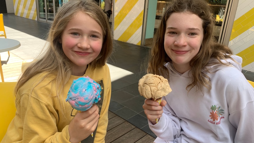 Shona's daughters, two tween girls with long brown hair, are sitting down, each holding an ice-cream cone.