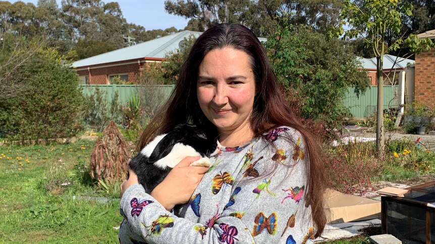 A woman with dark hair holding a black and white bunny, standing in a suburban backyard.