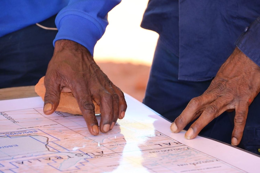 Close up of hands of traditional owners on a map at Lake Mackay.