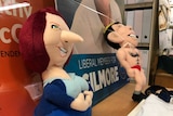 Soft dog toy of Julia Gillard with a very long and point nose in the foreground and another toy of Tony Abbott in red swimmers.
