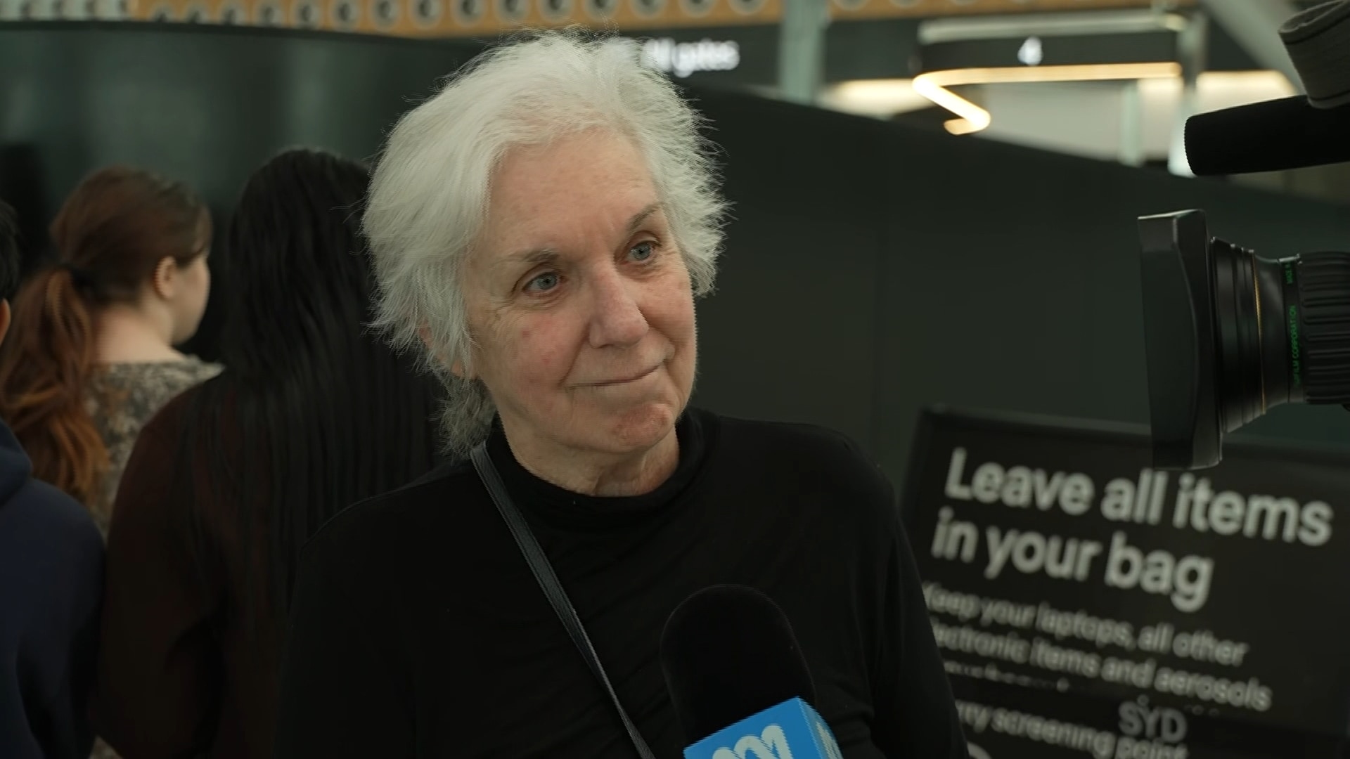 Sue Hobley smiling, speaking to a camera, with a blue ABC microphone to the side. She has white hair and wears a black jumper.