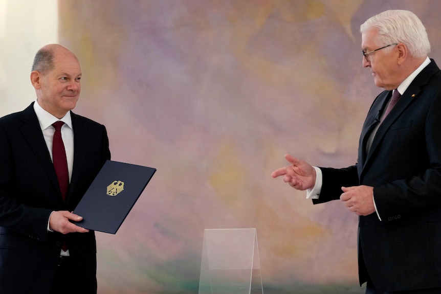 Olaf Schultz de pie a la izquierda, sosteniendo la carta de nombramiento que le dio Frank-Walter Steinmeier, de pie a la derecha.