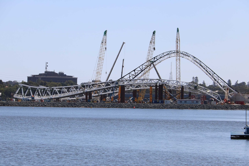 The Matagarup Bridge under construction over the Swan River, with steel arches and cranes rising into the sky.
