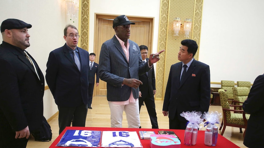 Dennis Rodman stands in front of a table and speaks to a North Korean official.
