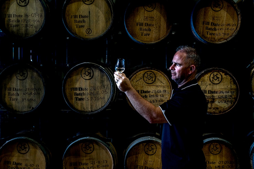 Man stands in front of timber barrels holding gin glass.