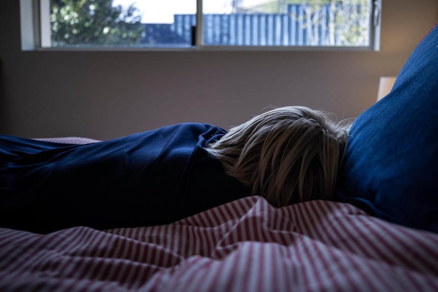 Young boy lying on his bed sad